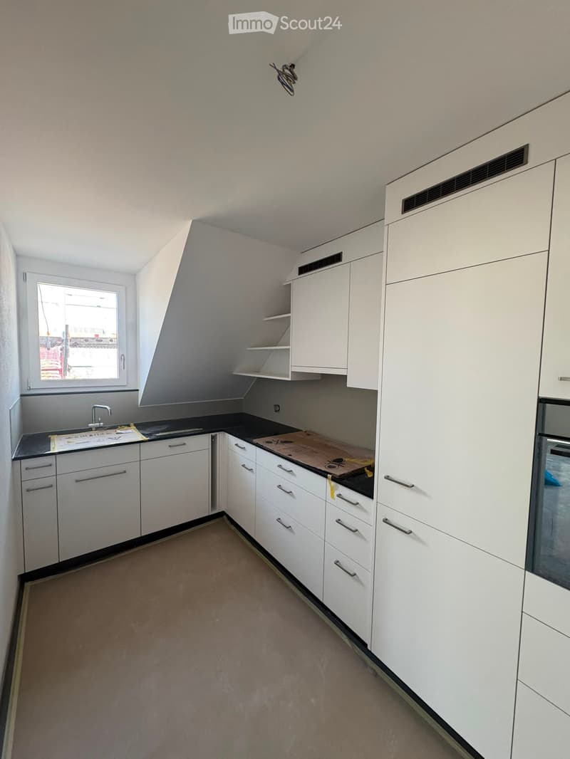 Empty kitchen with white cabinets, black countertops, and a window. No appliances or furniture are present.