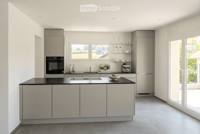 Modern kitchen with white cabinets, stainless steel appliances, and a black countertop. Features include a refrigerator, oven, sink, coffee maker, and decorative vases.