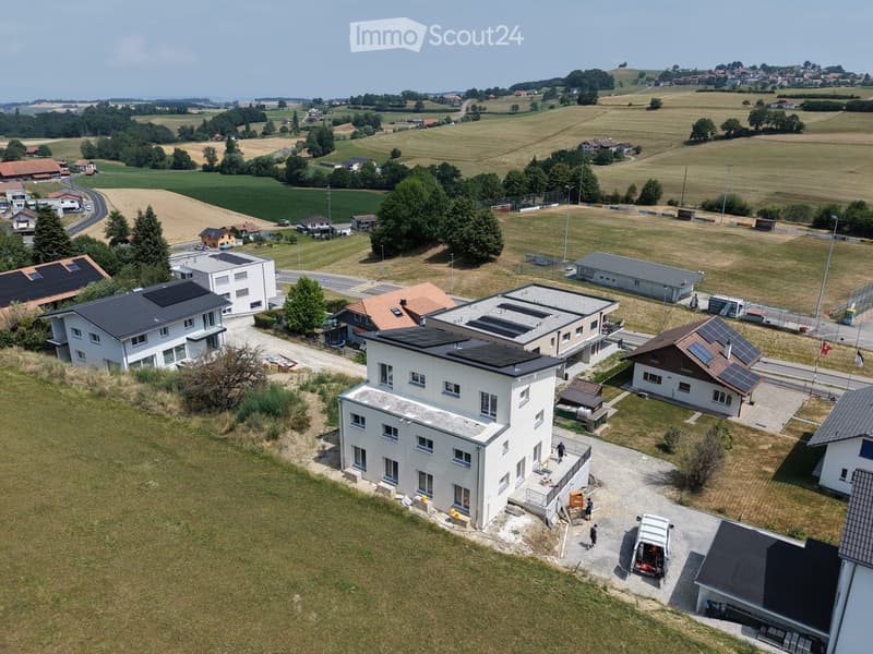 Aerial view of a residential area with multiple houses, solar panels on roofs, and surrounding green fields.