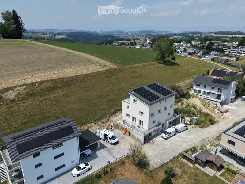 Aerial view of a modern two-story house with solar panels on the roof, surrounded by a spacious driveway with parked cars and a garage.