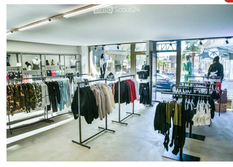 A modern clothing store interior with multiple clothing racks displaying various garments, mannequins, and large glass windows showing the street outside.