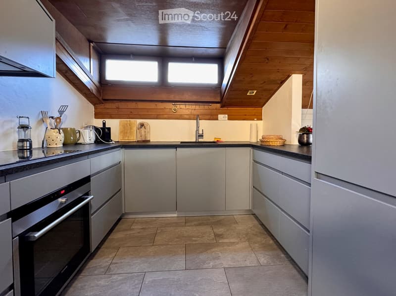 Modern kitchen with stainless steel appliances, wooden ceiling beams, and natural light from skylights. Includes an oven, faucet, cutting boards, and various kitchen utensils on the counter.