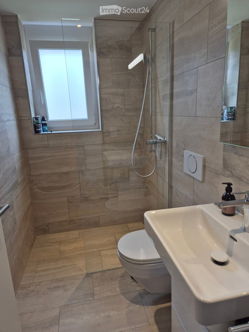 Modern bathroom with beige tiles, a toilet, a sink with a modern faucet, a shower with a glass enclosure, and a mirror above the sink.