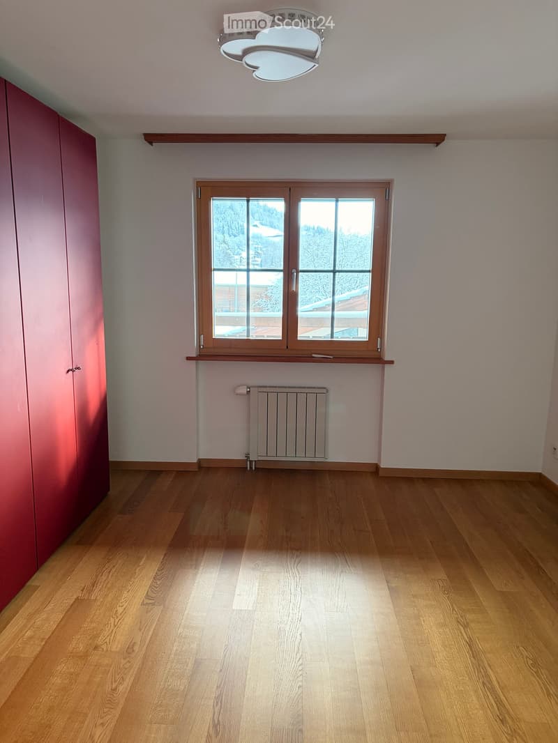 Empty room with wooden flooring, large window with wooden frame, radiator, and built-in closet with pink doors.
