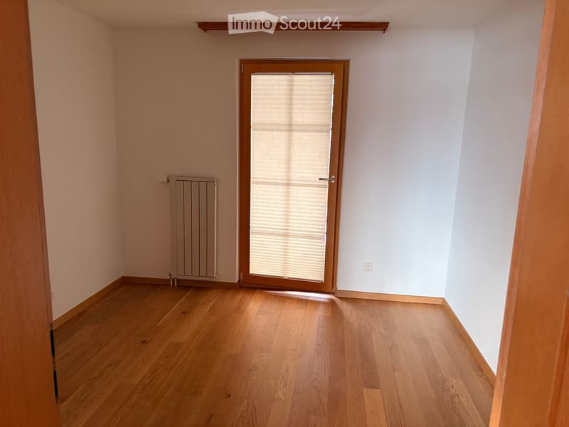 Empty room with wooden flooring, white walls, a radiator, and a window with blinds.