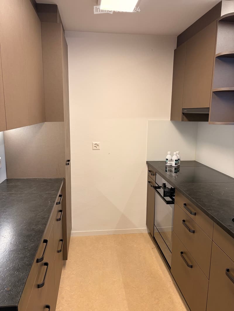 Modern kitchen with light wood cabinets, dark granite countertops, and a sleek design.