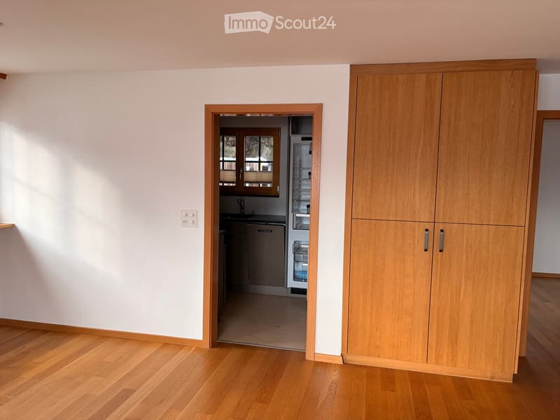 A hallway with wooden flooring and white walls, leading to a kitchen area with a refrigerator and dishwasher visible.