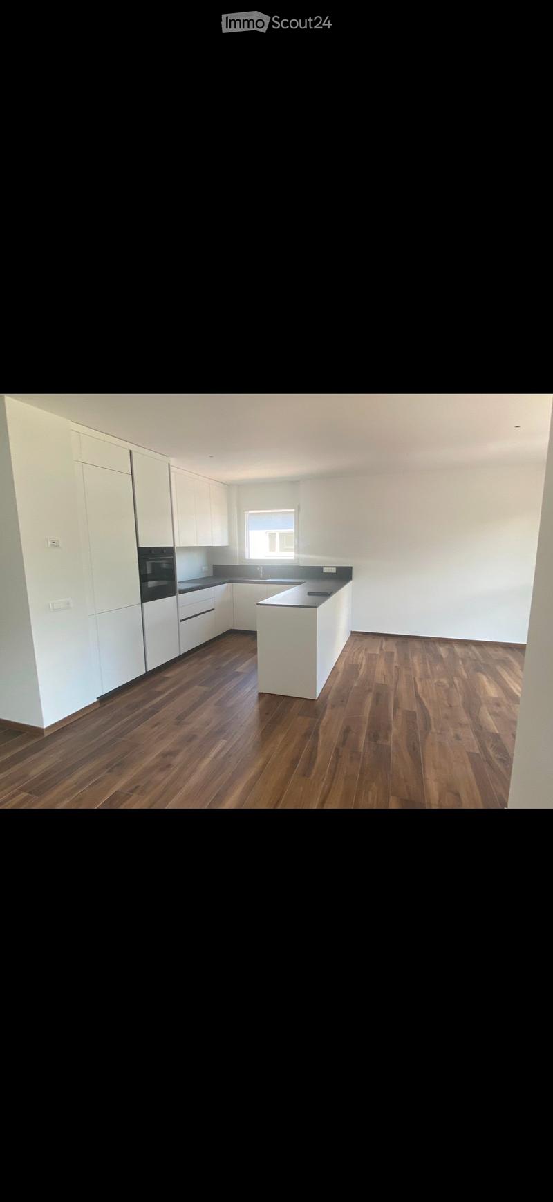 Empty kitchen with white cabinets, dark countertops, and wooden flooring. No appliances or furniture are present.