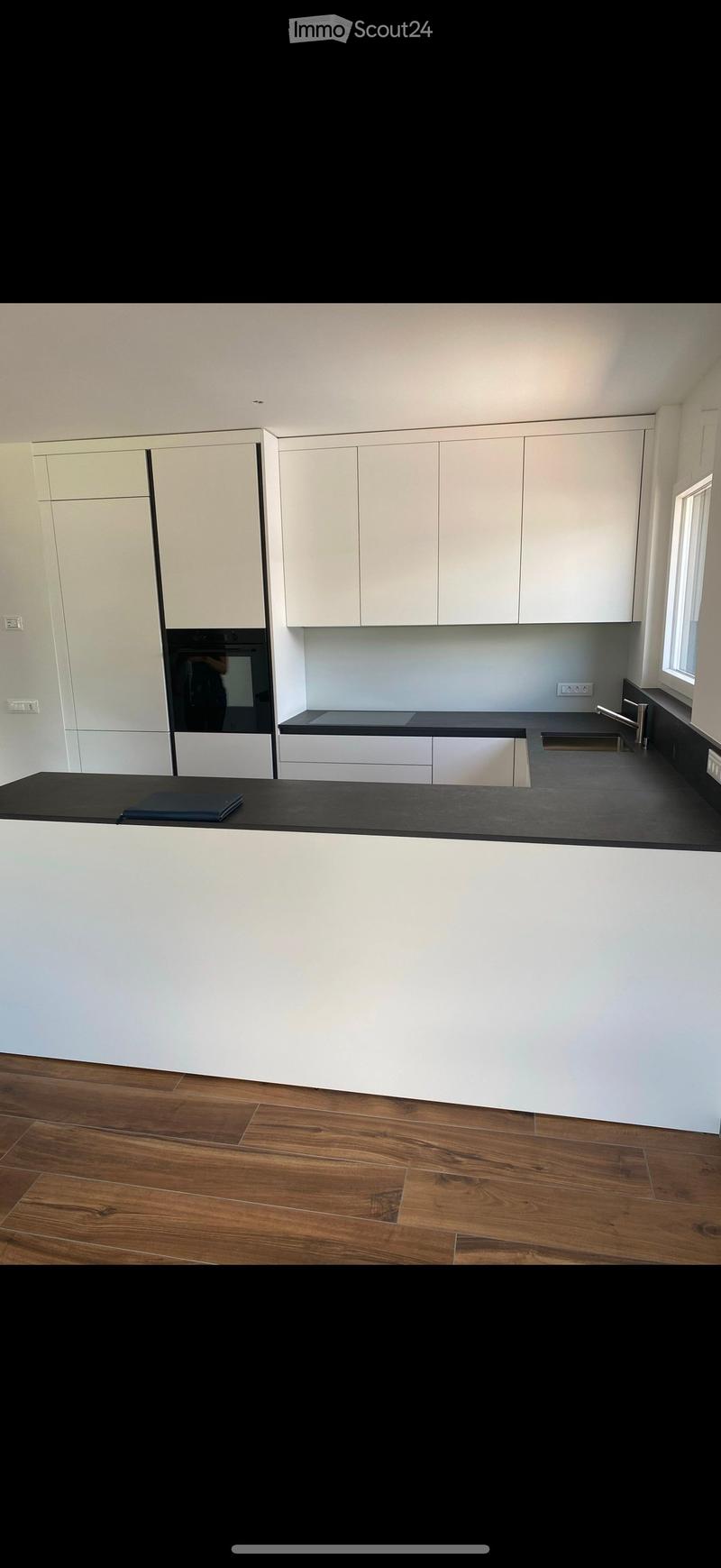 Modern kitchen with white cabinets, black countertops, and a wooden floor. Features a sink, faucet, and an oven.