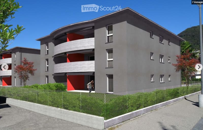 Modern multi-story residential building with grey facade, red accents, balconies, and surrounding greenery.