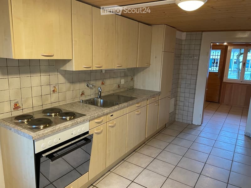 Modern kitchen with light wooden cabinets, granite countertop, electric stove, oven, and sink. The backsplash features decorative fruit tiles.