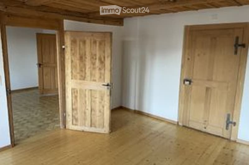 Empty room with wooden floors and white walls, featuring two wooden doors and a visible doorway in the background.