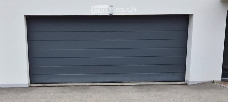 Modern grey garage door on a white building exterior, with a small light fixture above.
