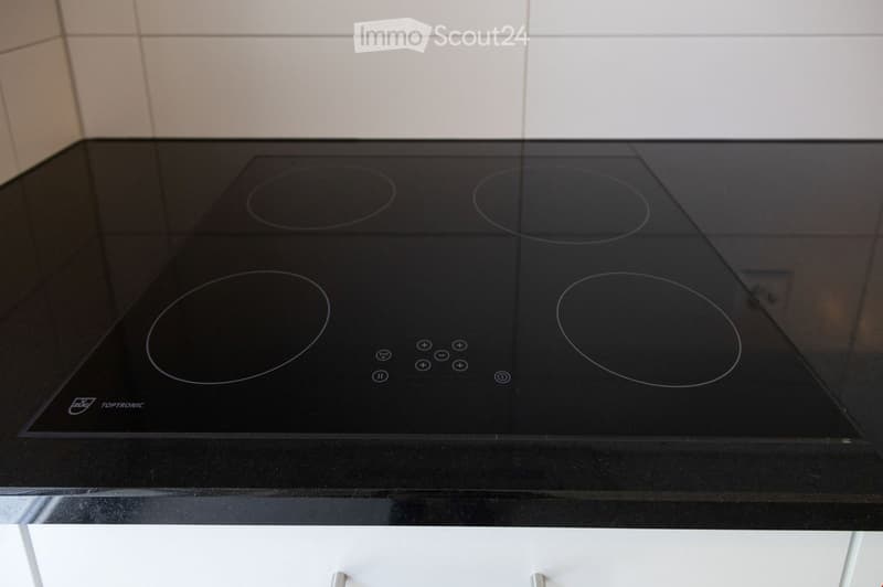 Modern black induction cooktop with four circular cooking zones and control buttons, mounted on a black countertop.
