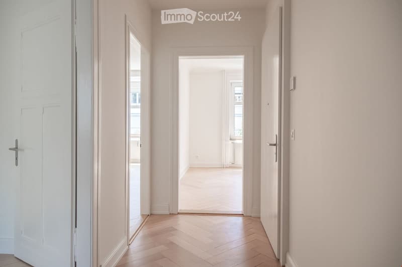 Empty hallway with light wooden flooring, white walls, and multiple doors leading to other rooms.
