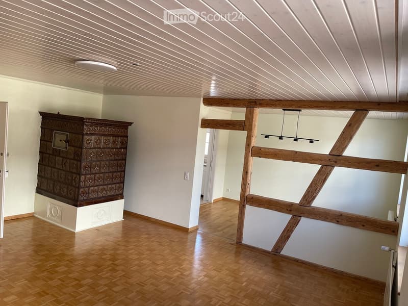 Empty room with wooden flooring, white walls, exposed wooden beams, and a decorative cabinet on the left side.