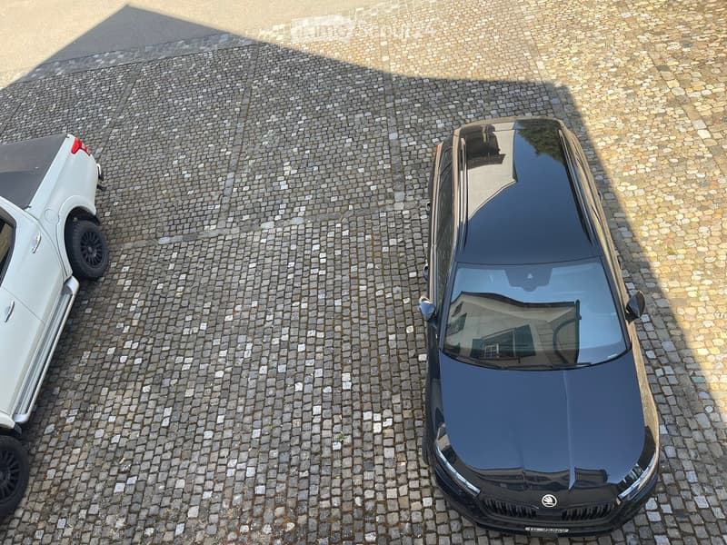 Two cars parked on a cobblestone surface, one white and one black.