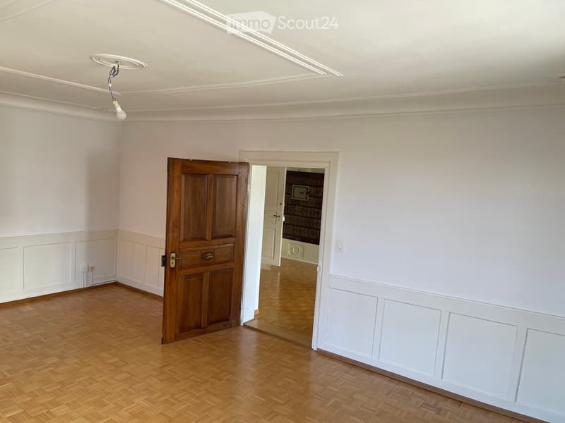 Empty room with wooden flooring, white walls, and a wooden door leading to another room.