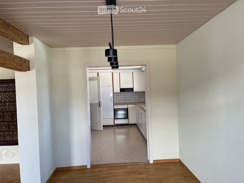 Bright hallway with wooden flooring, white walls, and a visible kitchen area with white cabinets, stainless steel appliances, and a tiled backsplash.