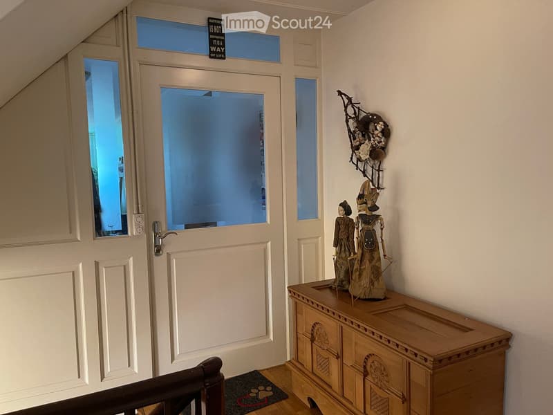 Hallway with a wooden cabinet, decorative items, and a door leading to another room.