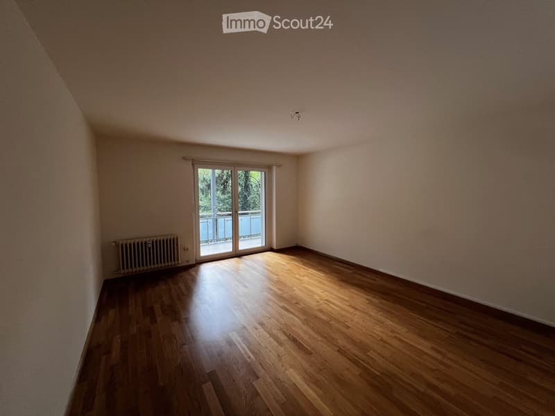 Empty room with wooden flooring, white walls, and a sliding glass door leading to a balcony.