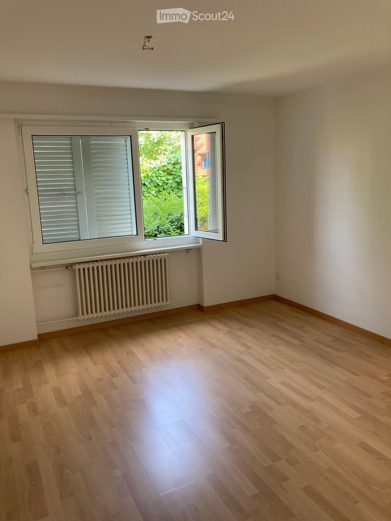 Empty room with wooden flooring, white walls, and a window with shutters and radiator below.