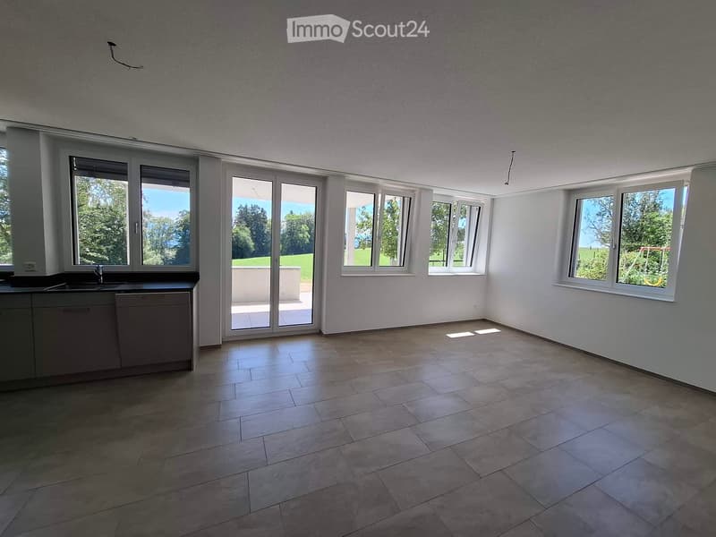 Empty room with tiled floor, white walls, large windows, and a sliding glass door leading to a balcony.