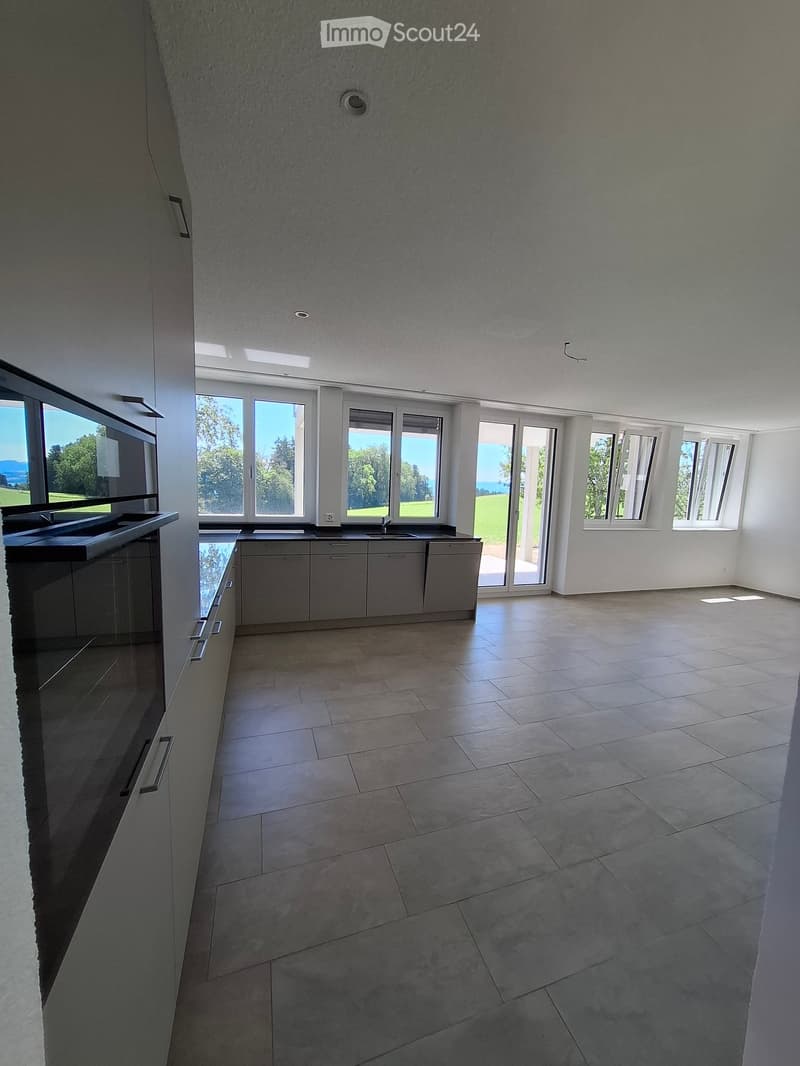Empty kitchen with modern cabinetry, large windows, and a tiled floor. No furniture or appliances are present.