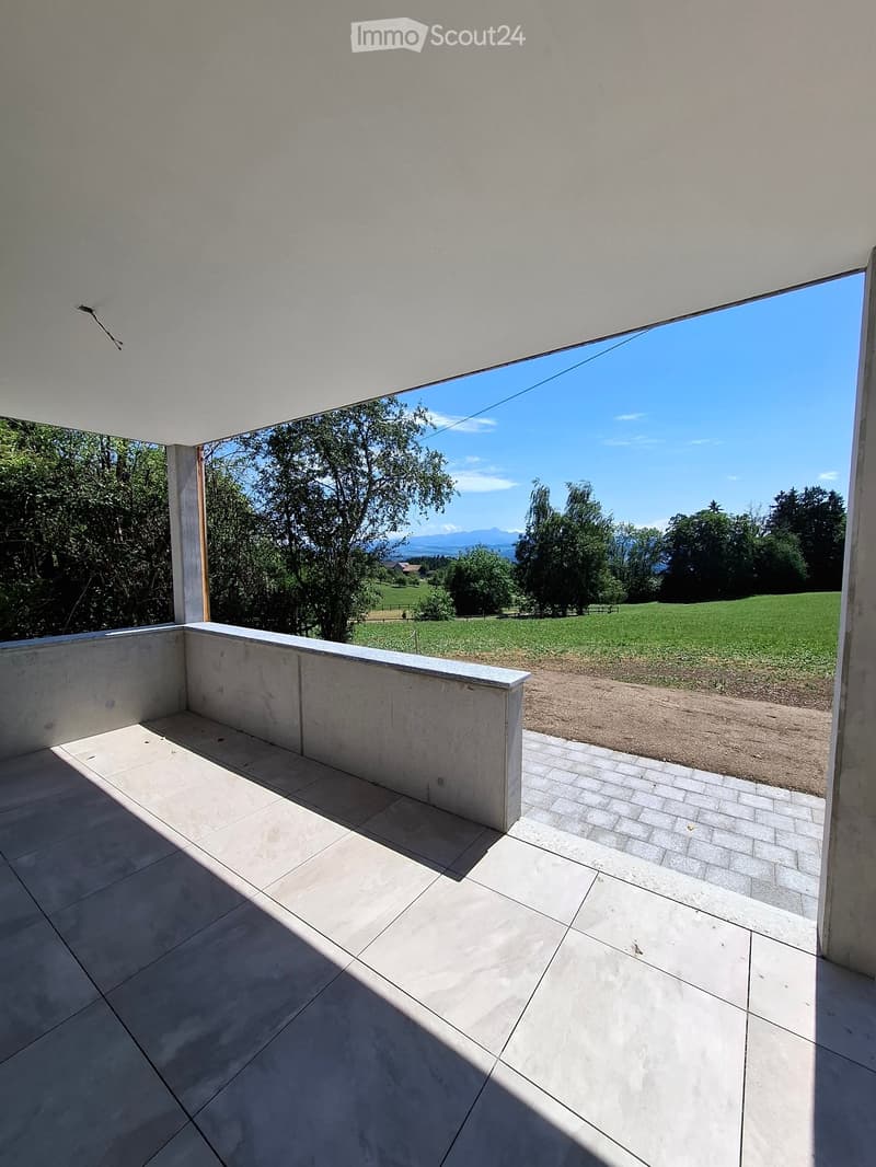 Modern balcony with tiled floor, white railing, and expansive view of green fields and trees under a clear blue sky.