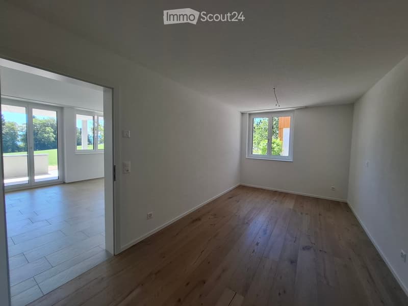Empty room with wooden flooring, white walls, and large windows, including a sliding glass door leading to an outdoor area.