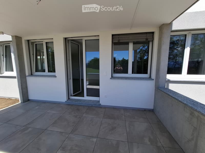 Balcony with tiled floor, white walls, large windows, and sliding glass doors leading to the interior.