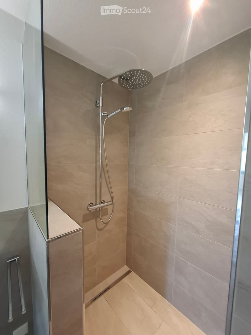 Modern shower area with beige tiles, a handheld showerhead, and a fixed overhead showerhead.