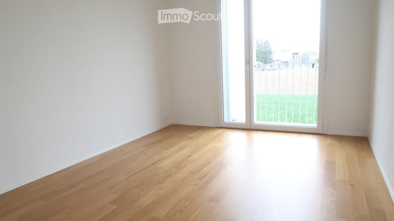 Empty room with light wooden flooring and white walls, featuring a large sliding glass door leading to a balcony or outdoor area.
