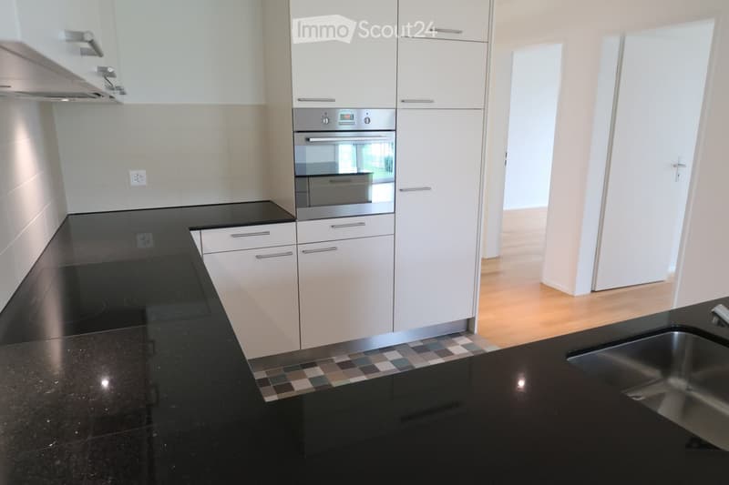 Modern kitchen with white cabinets, black countertops, and stainless steel appliances, including an oven and sink.