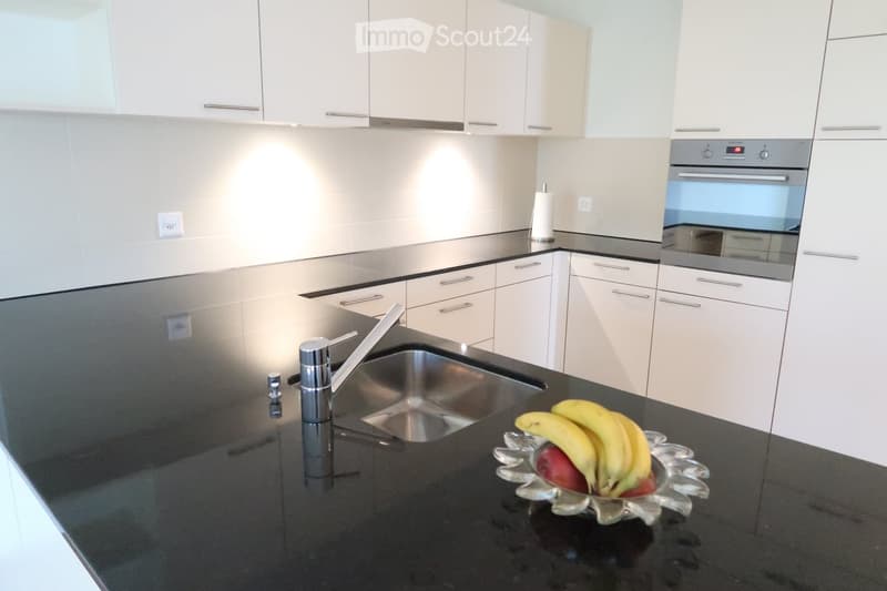 Modern kitchen with white cabinets, black granite countertop, stainless steel sink and faucet, and a bowl of fruit on the counter.