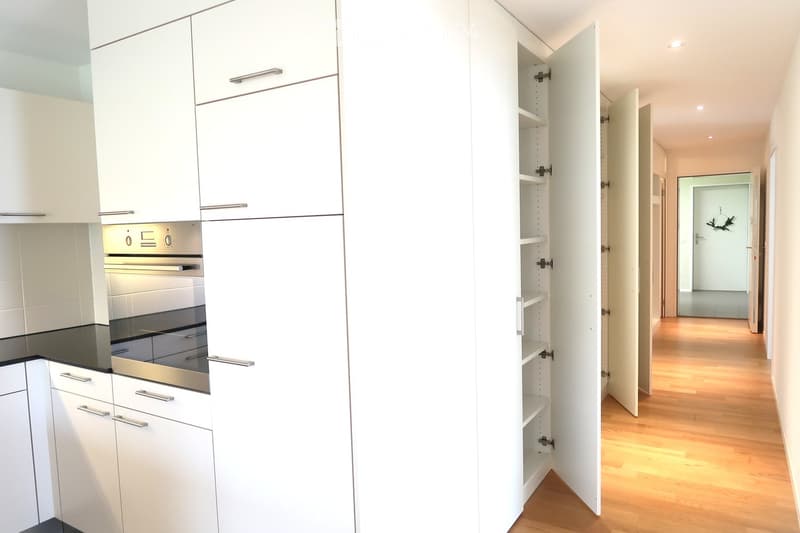Modern kitchen with white cabinets, stainless steel oven, and open shelving unit.