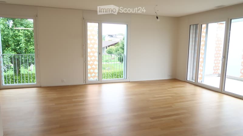 Empty room with wooden flooring, large sliding glass doors leading to a balcony, and white walls.