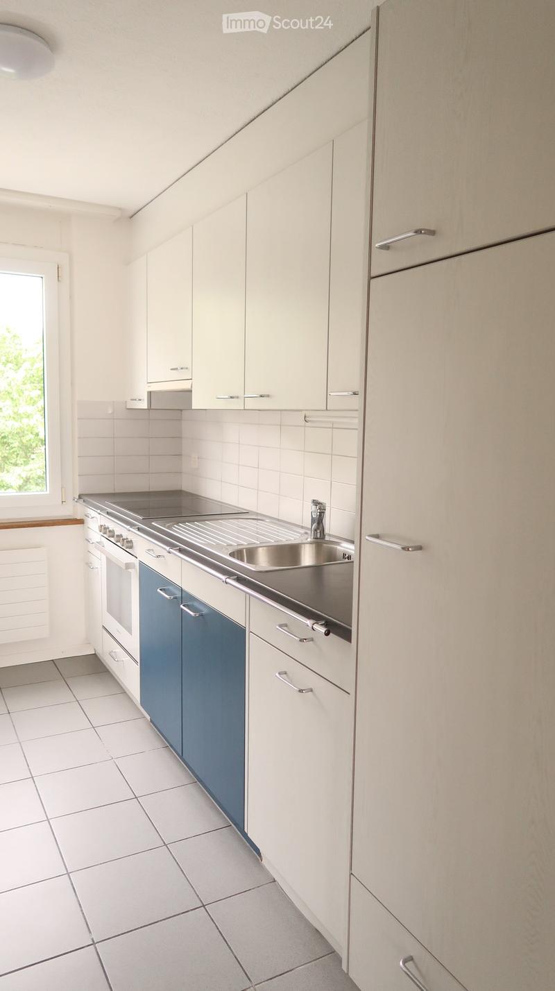 Modern kitchen with white cabinets, stainless steel sink, oven, and tiled floor.
