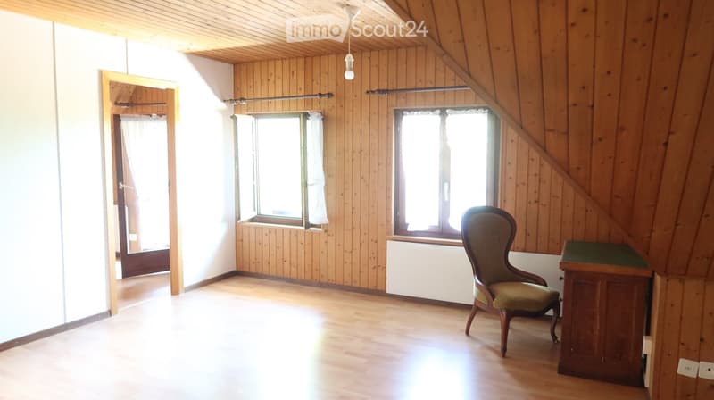 room with wooden walls, wooden floor, a white wall with two windows, a chair, and a cabinet
