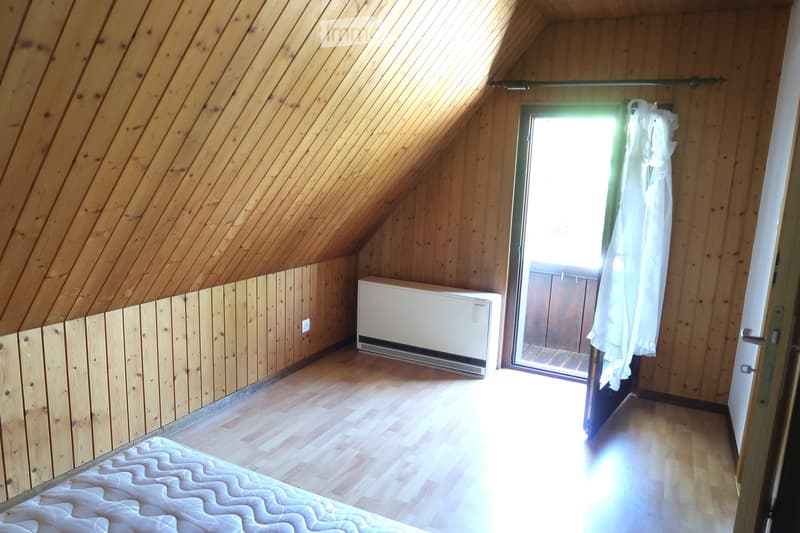 room with wooden walls, wooden floors, single bed, white door, small window, small balcony