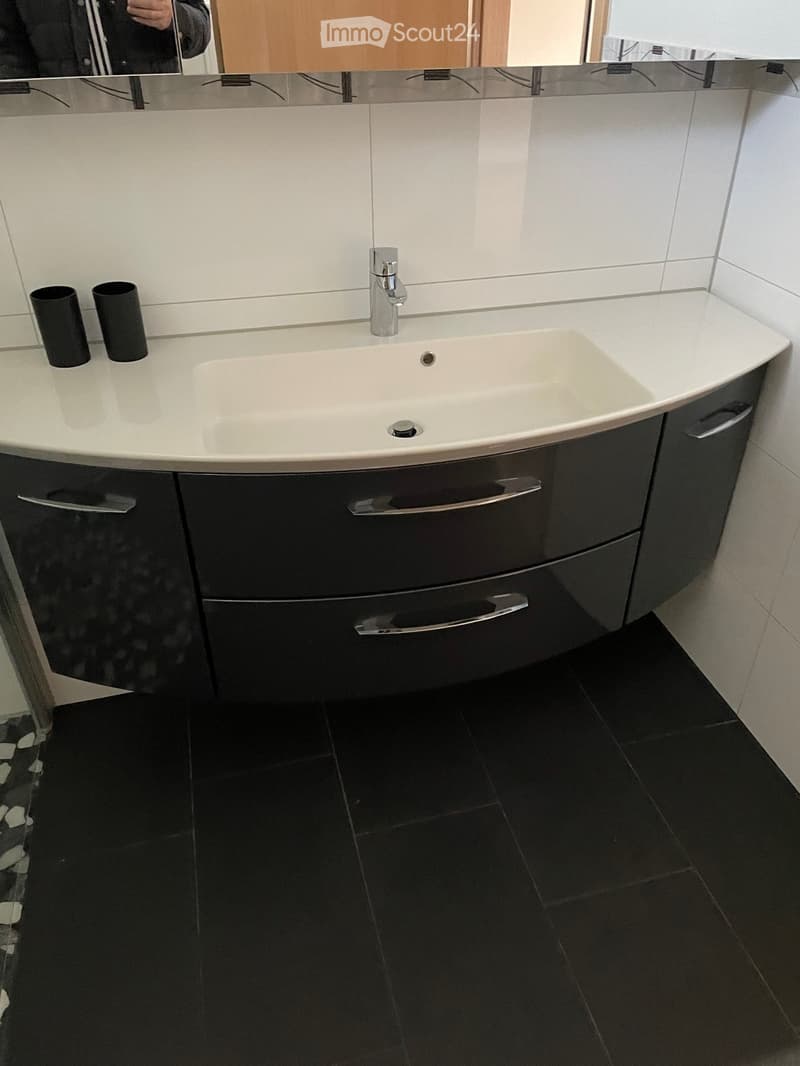 Modern bathroom with a white sink, chrome faucet, dark grey cabinet, and two black cylindrical containers on the counter.