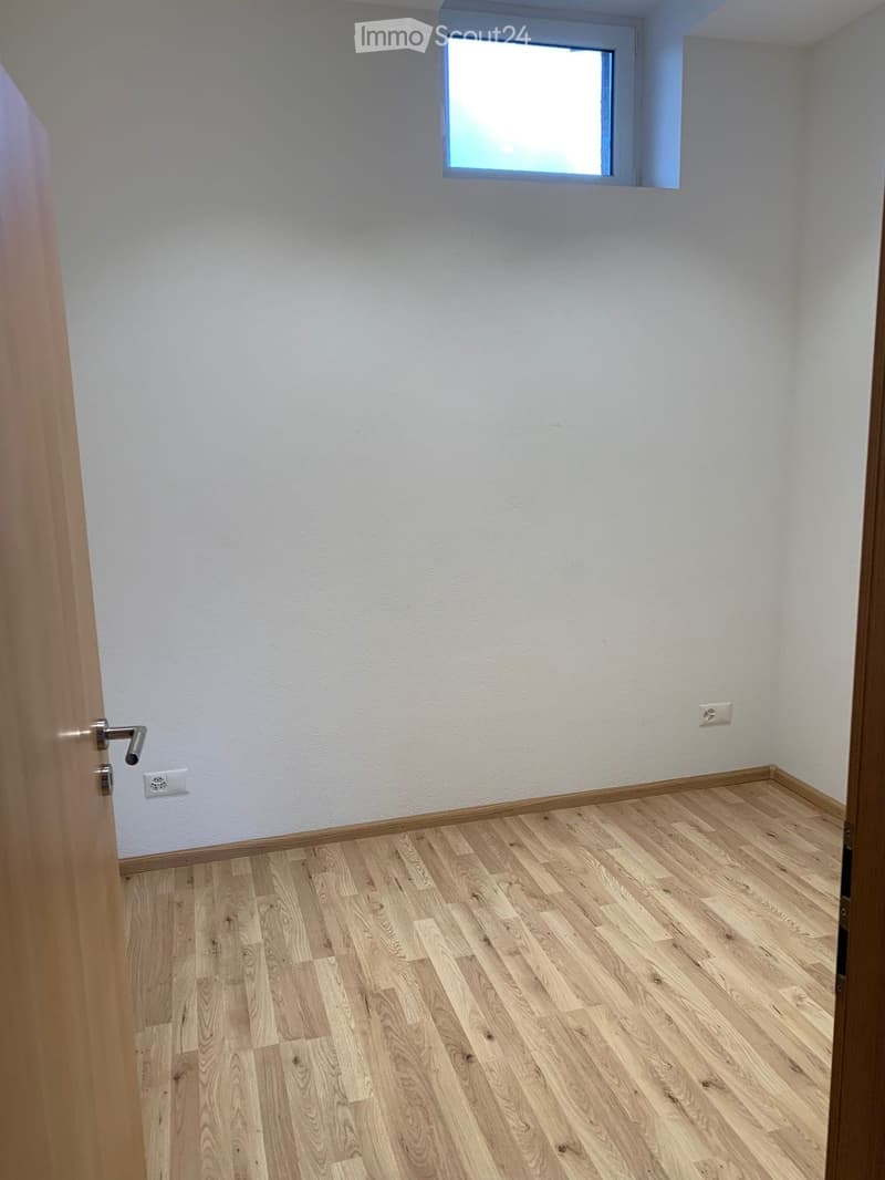 Empty room with light wooden flooring, white walls, and a small window letting in natural light.