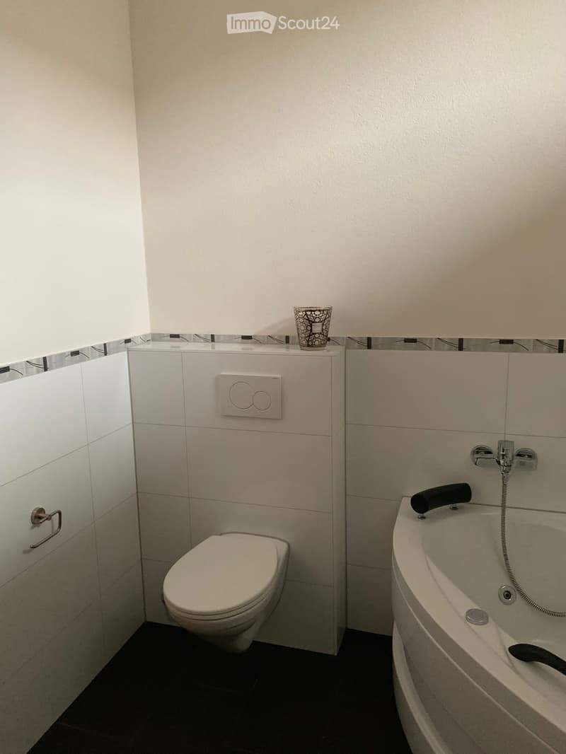 Modern bathroom with white tiled walls, a toilet, a bathtub, and a small decorative cup on the edge of the bathtub.