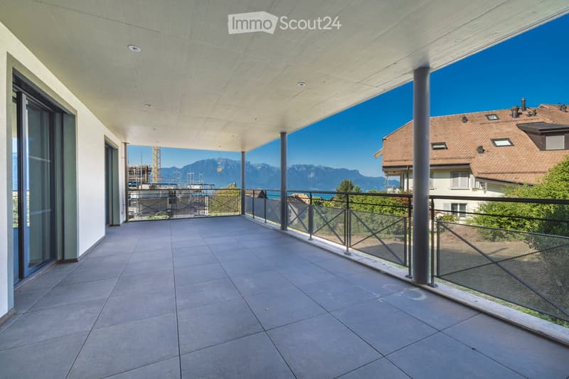 Modern balcony with tiled floor, glass railing, and a view of mountains and a lake.