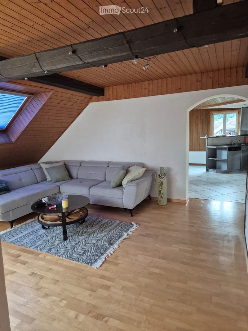 Living room with wooden floors, slanted wooden ceiling, grey sectional sofa, coffee table, and a vase on the floor.
