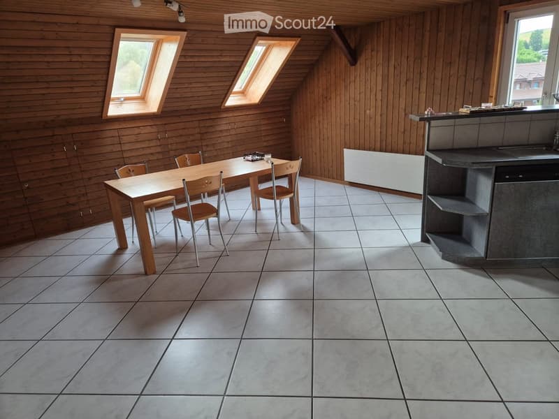 Bright, wooden-paneled room with a dining table and chairs, a modern kitchen counter, and large windows including skylights.
