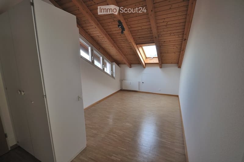 Empty room with wooden flooring, white walls, exposed wooden ceiling beams, and skylight windows.