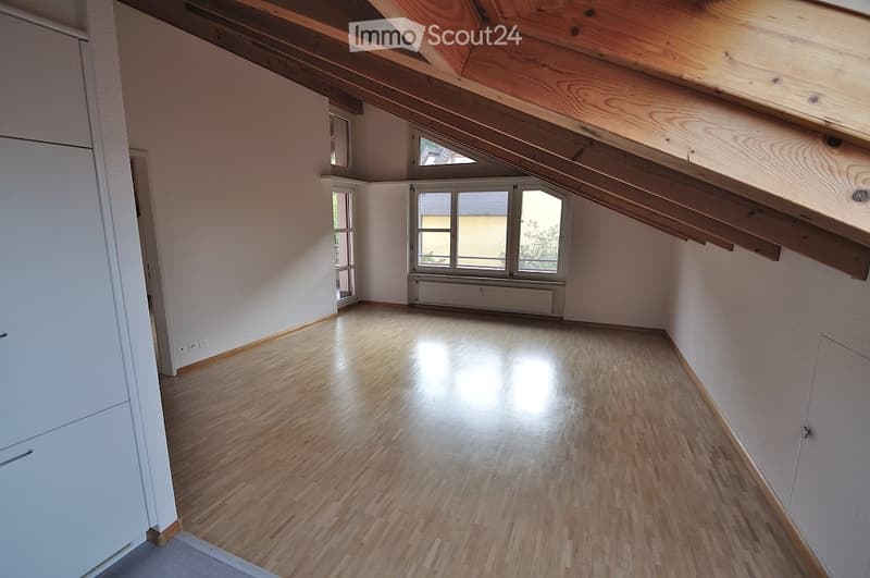 Empty attic room with wooden floors, exposed wooden beams, and large windows allowing natural light.