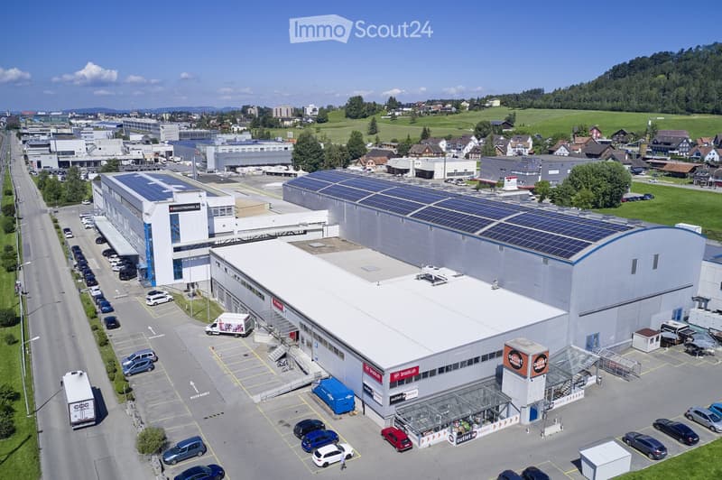 Aerial view of an industrial park with multiple large buildings, solar panels on rooftops, and a parking lot filled with cars.