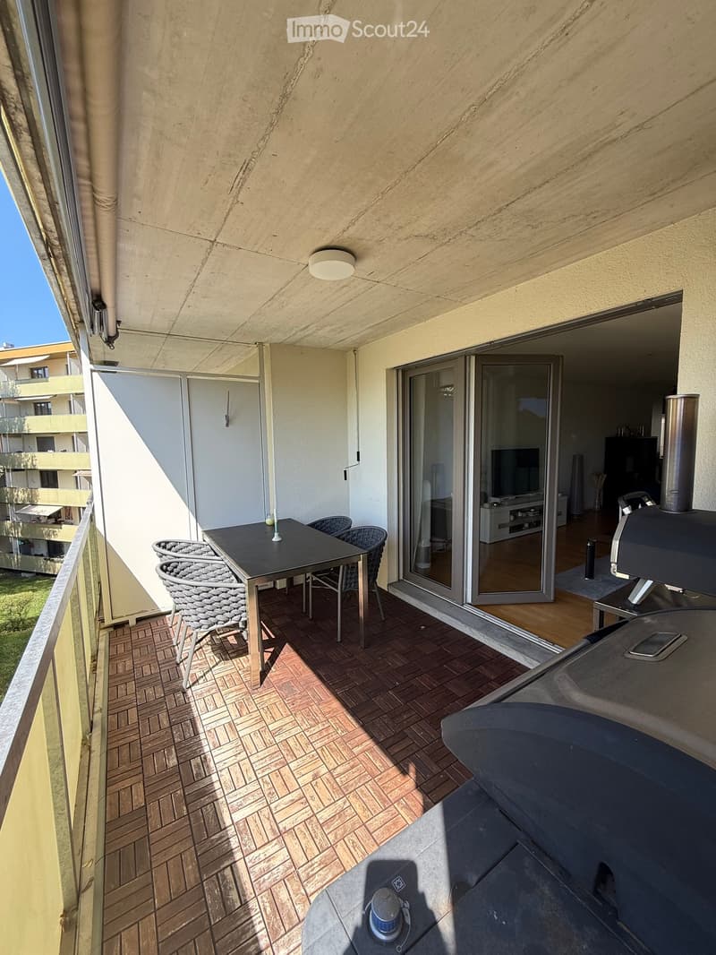 Balcony with tiled floor, outdoor table and chairs, sliding glass doors leading to interior space.